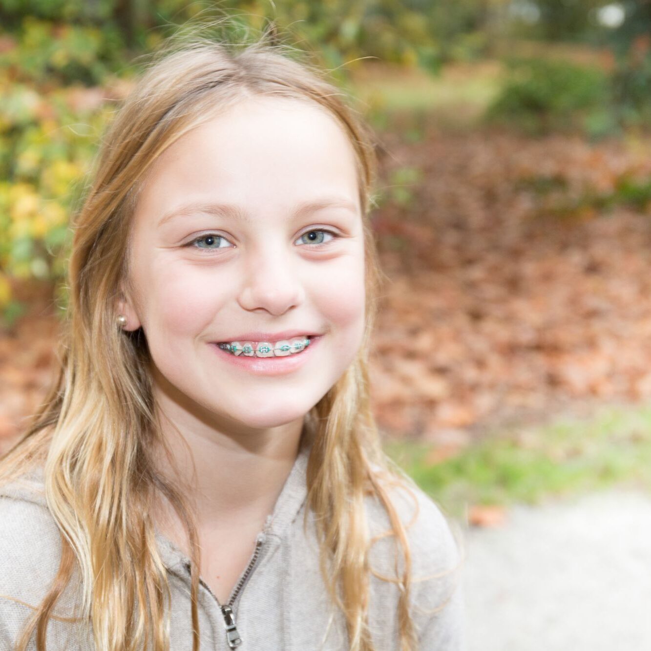 Smiling girl with metal braces outdoors, showcasing orthodontic treatment by McHugh Orthodontics in Moorestown.