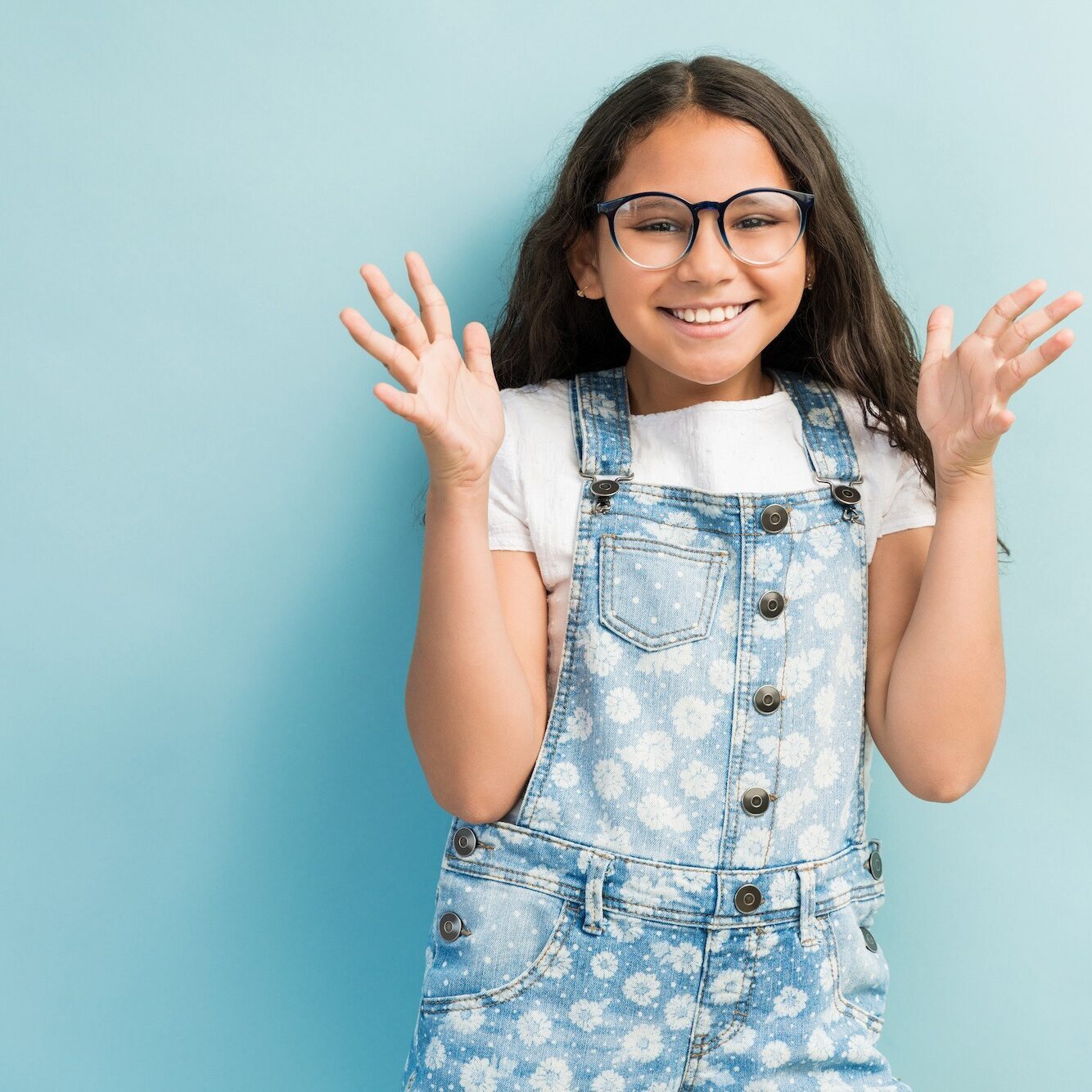Smiling girl in denim overalls and glasses, showcasing a confident expression, representing the positive experience of orthodontic treatment at McHugh Orthodontics in Moorestown.